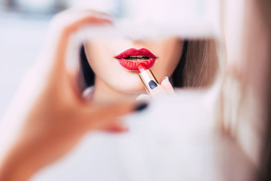 Mujer pintando sus labios de rojo frente al espejo