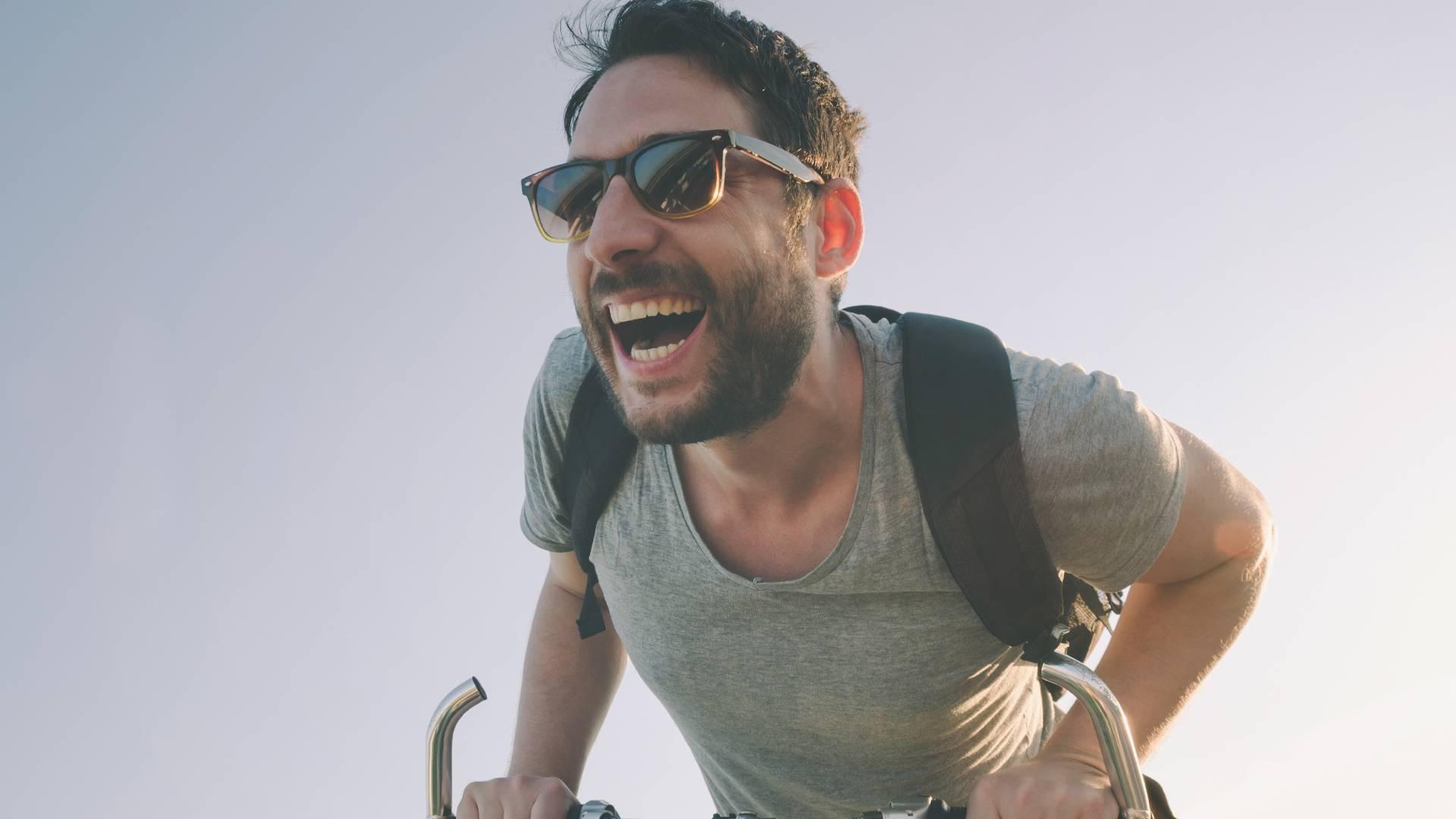 Hombre manejando bicicleta mientras sonríe con lentes oscuros