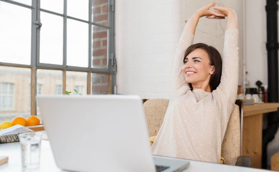 Mujer estirando los brazos hacia arriba mientras trabaja en su computadora sonriendo