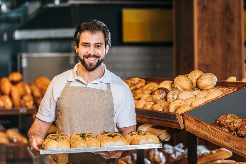 Hombre experto en panadería delante de un horno lleno de panes