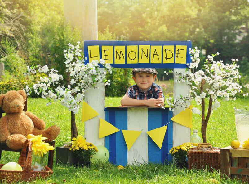 Niño con un puesto de limonadas en un jardín