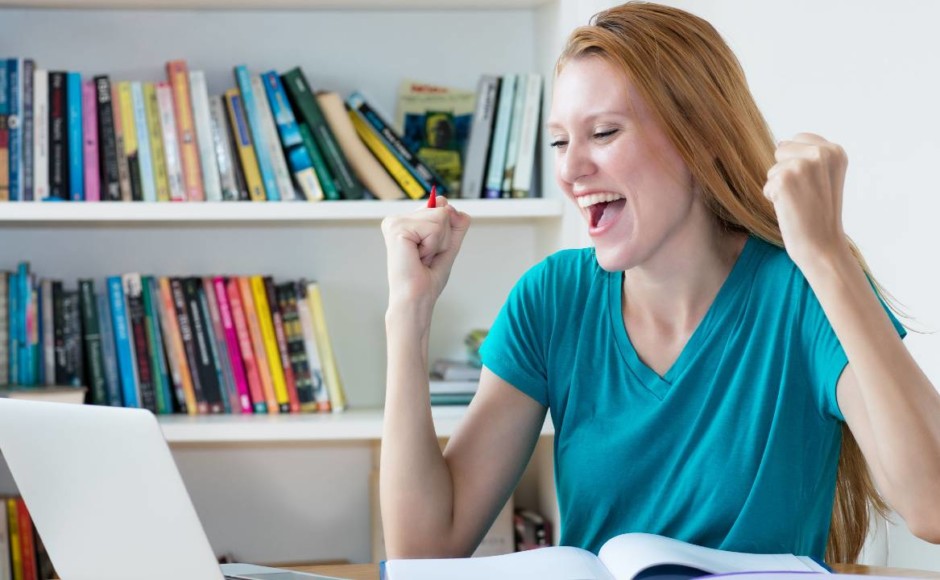 Mujer celebrando mientras estudia en línea en su computador portátil