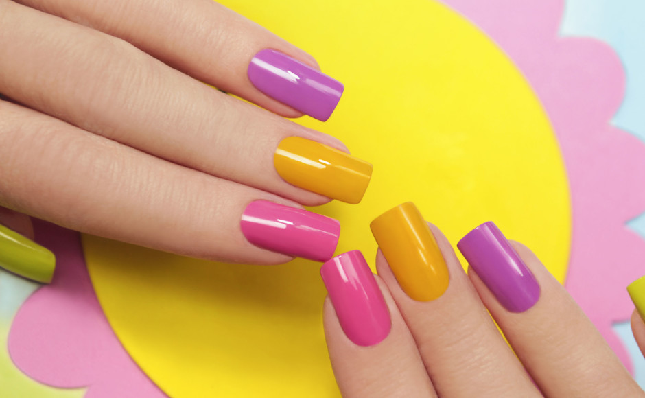 Manos de una mujer con uñas acrílicas de colores morado, amarillo y rosado