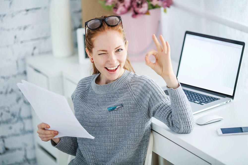 mujer feliz usando un computador, sosteniendo una hoja