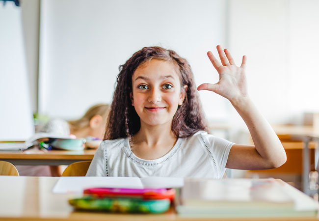 foto de un niño levantando la mano para que le den permiso para hablar, con expresión entusiasmada