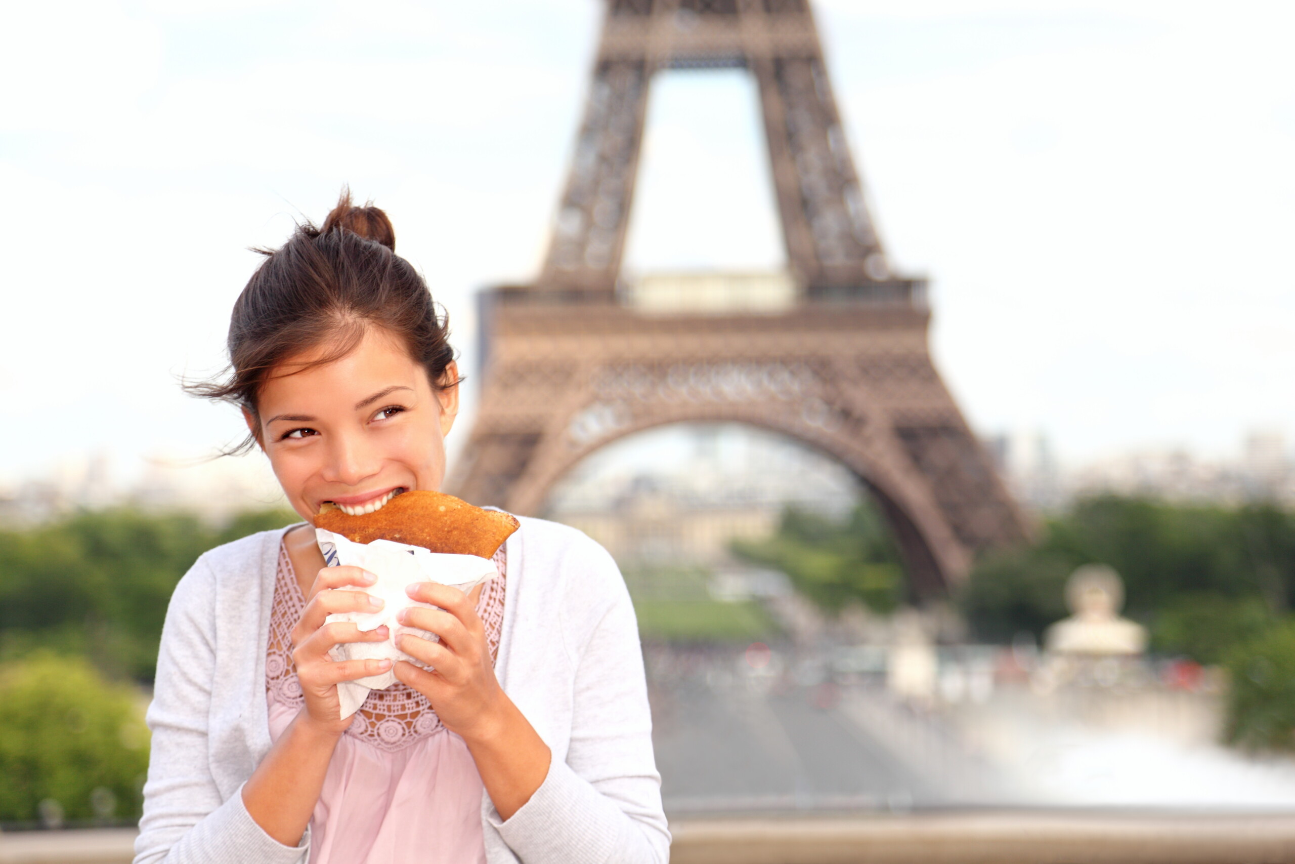 mujer comiendo un crepe frente a la torre eiffel