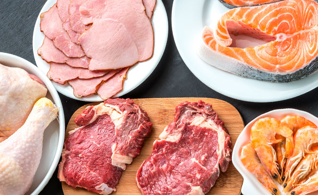 foto de una mesa con diferentes cuencos que contienen langostinos, carnes de res, de cerdo y pollo en forma separada, listos para ser cocinados