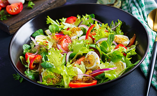 Un plato de ensaladas en el centro con otros platos alrededor repletos de otras verduras