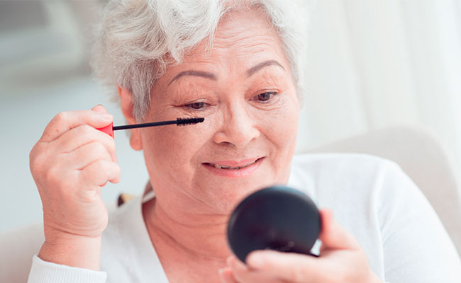 Mujer mayor de 60 maquillándose frente al espejo