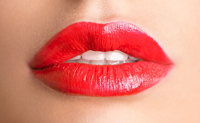 zoom a unos labios pintados perfectamente de rojo brillantes, que expresan una sonrisa