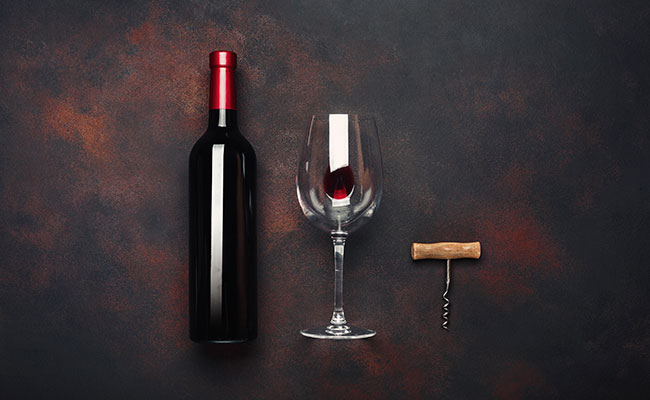Foto de una mesa con una botella de vino tinto, una copa servido y un destapador