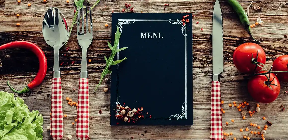 Imagen de un menú de restaurante, cubiertos, tomates y lechuga sobre una tabla